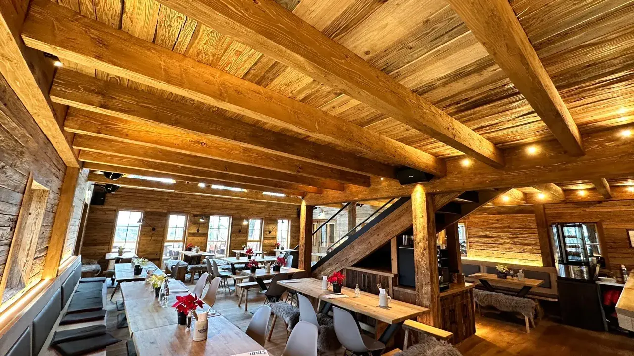 Gemütliches Holzinterieur eines Restaurants mit Holzbalken und Tischen.