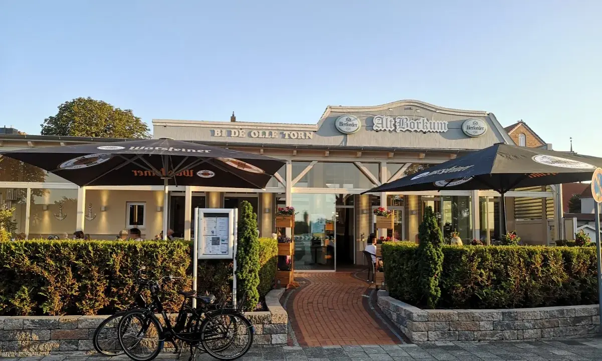 Zwei Fahrräder vor dem Restaurant "Alt Borkum" mit Sonnenschirmen und Büschen.