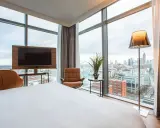 Modern Hotelzimmer mit Skyline-Blick, Bett, Sessel und Fernseher.