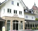 Gasthof Sasse in Soest mit Hotel & Gastronomie-Schild, Steinfassade und Kirche im Hintergrund.