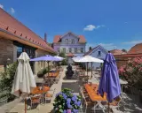 Terrasse eines Weinguts mit Tischen, Stühlen, Sonnenschirmen und Blumen unter blauem Himmel.