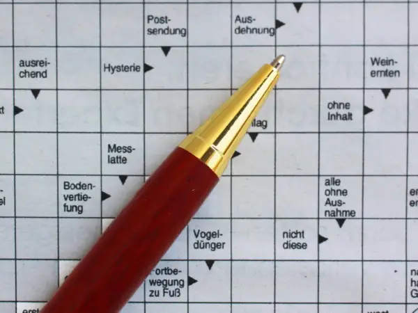 Ein roter Stift liegt auf einem Kreuzworträtsel mit deutschen Begriffen.